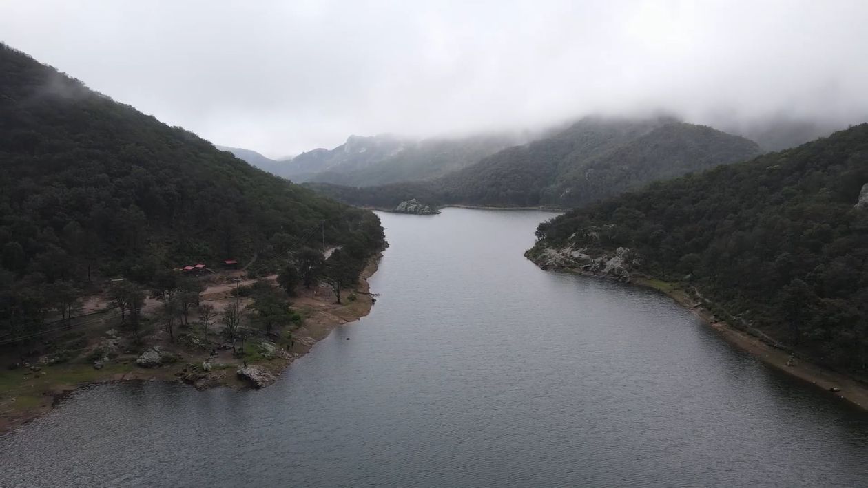 Ein nebliger Bergsee zwischen bewaldeten Hängen, aus der Luft aufgenommen.